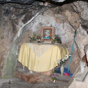 Photo of an altar at one of the fertility shrines. The altar has a yellow cloth draped over it with flowers and other items with religious imagery. The altar is surrounded by a rock formation.