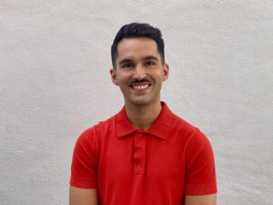 Daniel Valtueña stands in front of white wall. He has a mustache and wears a red shirt.